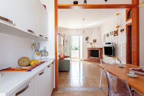 Una cocina con una licuadora, frutas y un comedor con mesa y sillas.