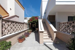 A narrow outdoor corridor with a staircase leading to a second floor, flanked by white walls and a decorative stone balustrade.