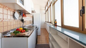 A narrow kitchen with a tiled backsplash, a sink, a refrigerator, and a window with blinds. - Casa Crystal Near The Sea - 5min Walk to San Foca (Melendugno)