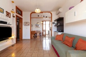A living room with a television, sofa, and orange cushions. There is a dining area with a table and chairs.