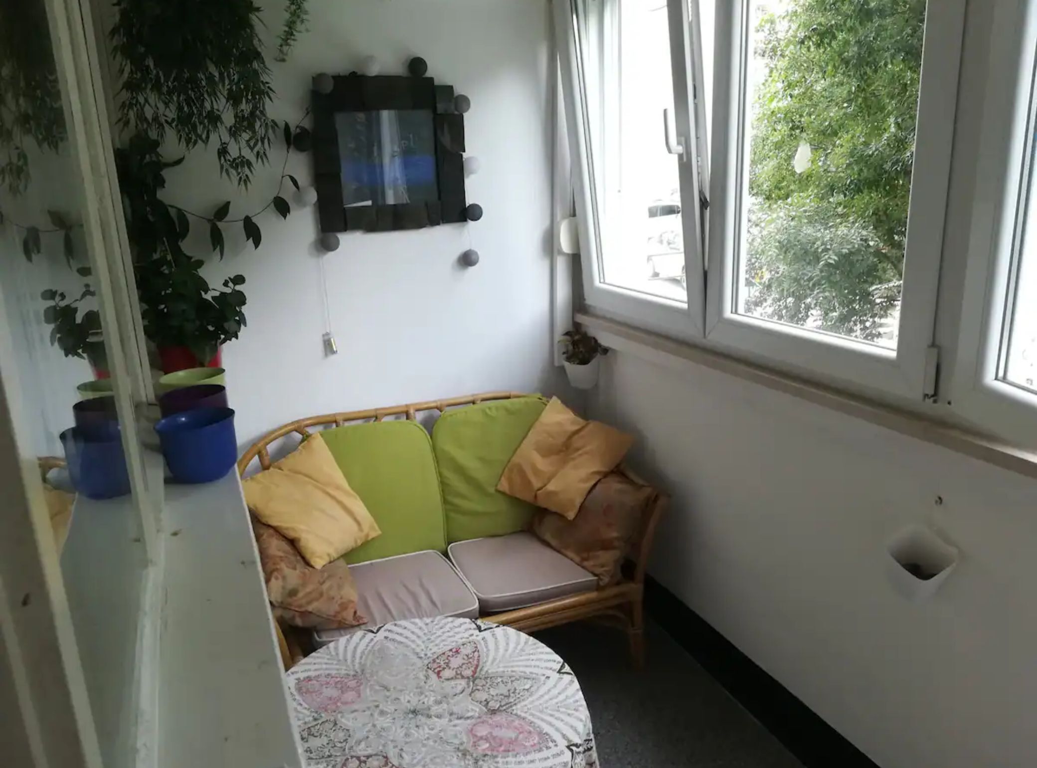 Une pièce d’angle avec un canapé en osier, une petite table ronde et une plante en pot.