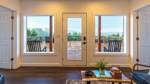 A room with a large wooden door leading to a deck with outdoor seating.