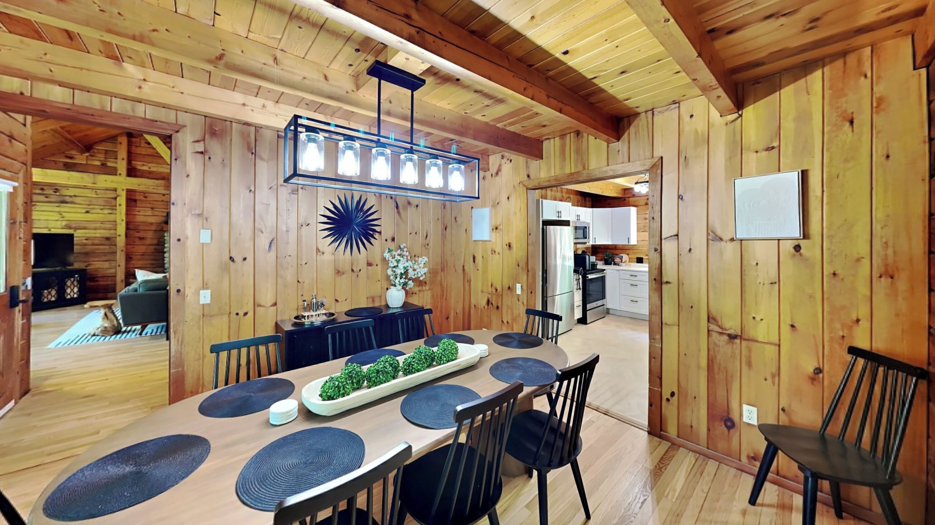 A wooden interior with a dining area featuring a long table, chairs, and a decorative centerpiece.