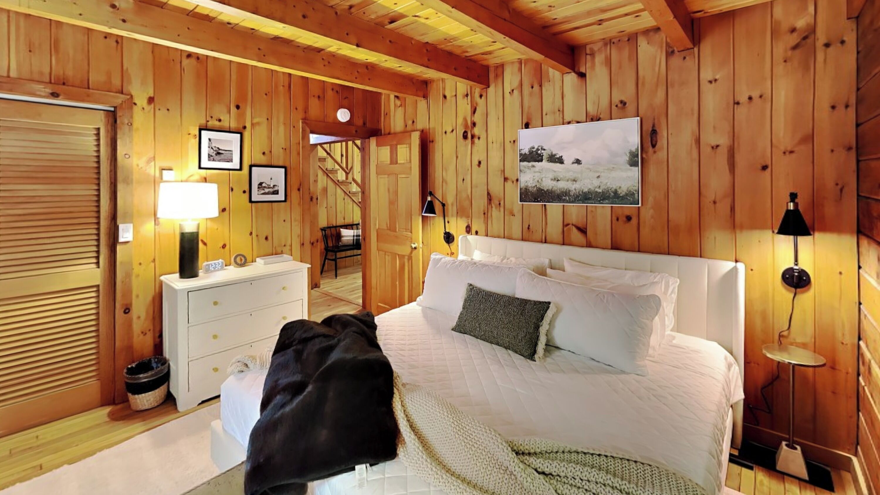 A wooden-paneled bedroom with a bed, bedside lamps, a nightstand, a dresser, and a framed picture on the wall.