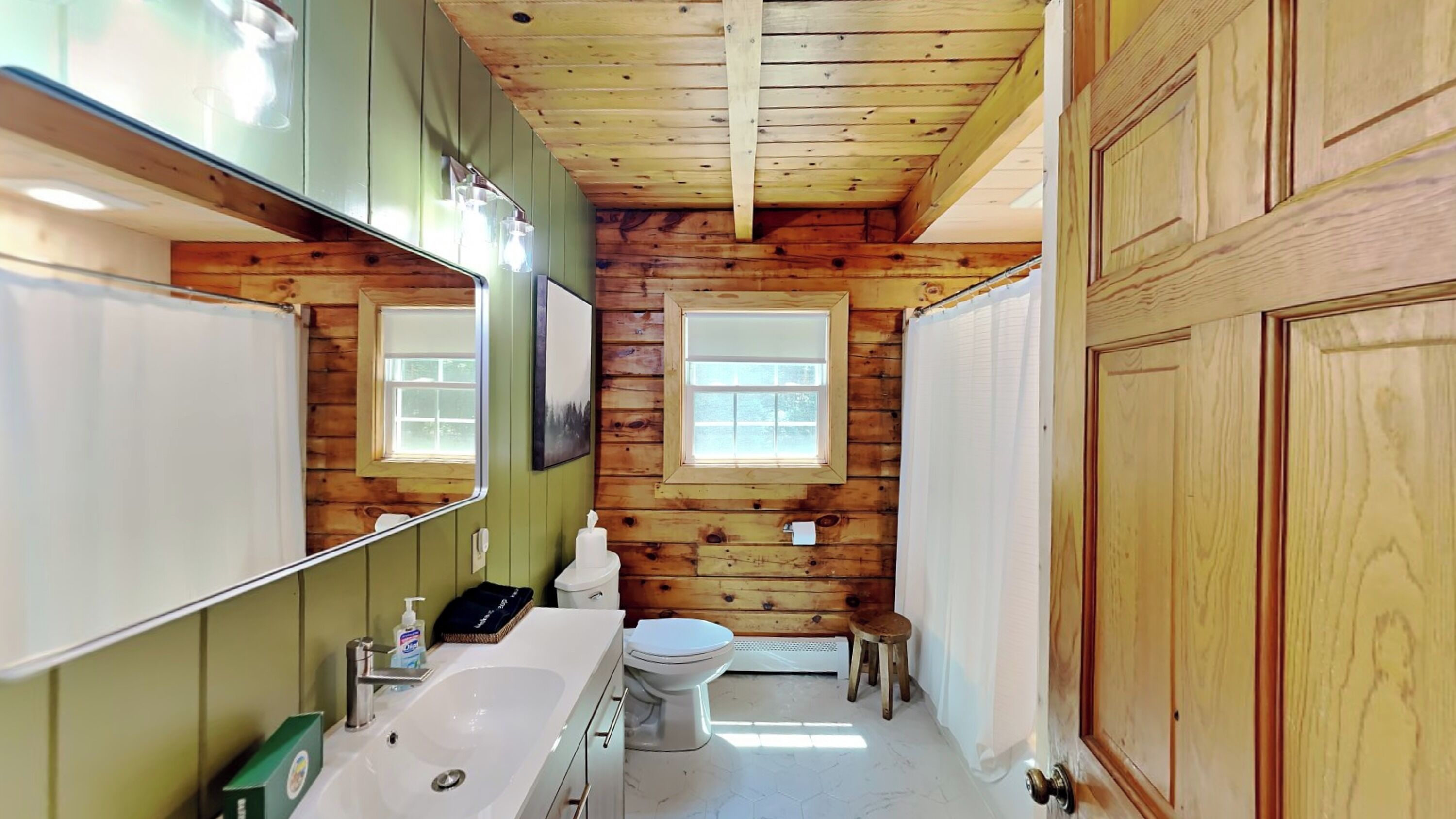 Un bagno in una cabina di legno con uno specchio grande, un lavandino, un water e una finestra.