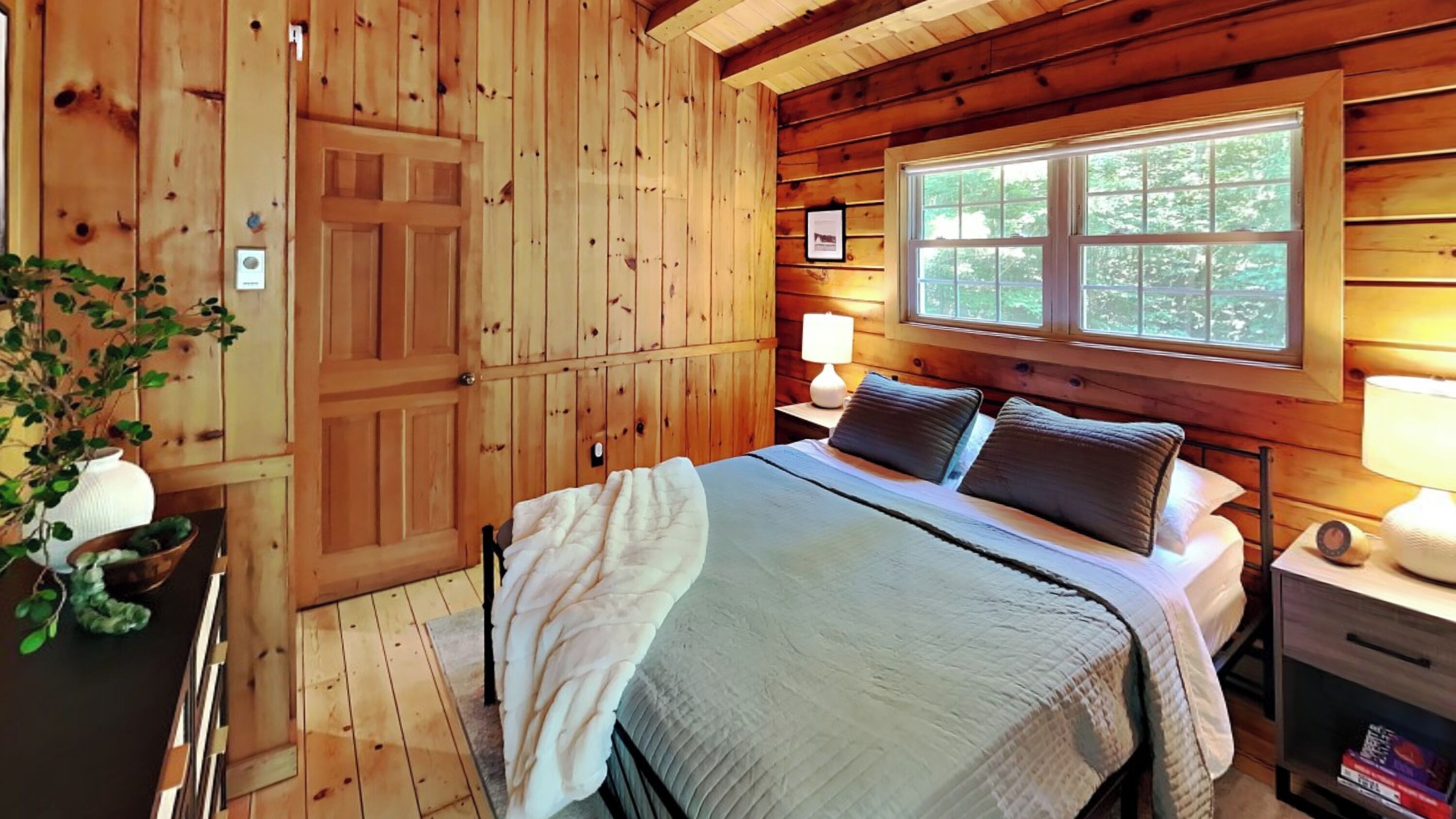 Une chambre dans une cabane en bois, avec un lit, des lampes de chevet, une fenêtre et une porte.