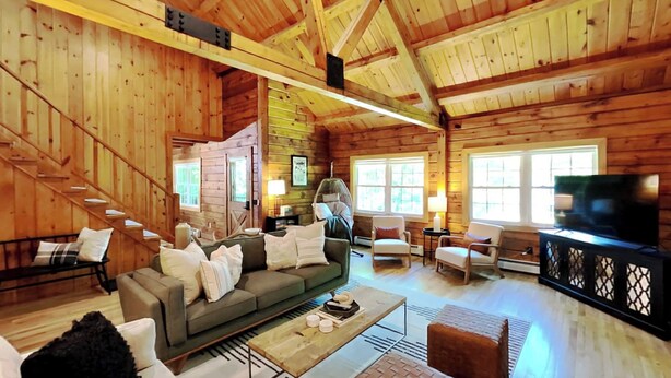 Ein gemütliches Blockhaus-Interieur mit einer Couch, Sesseln, einem Fernseher und einem Hängesessel.