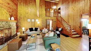 Ein Holzinnenraum mit Kamin, einer Treppe und einer Sitzecke mit einer Couch und Sesseln.