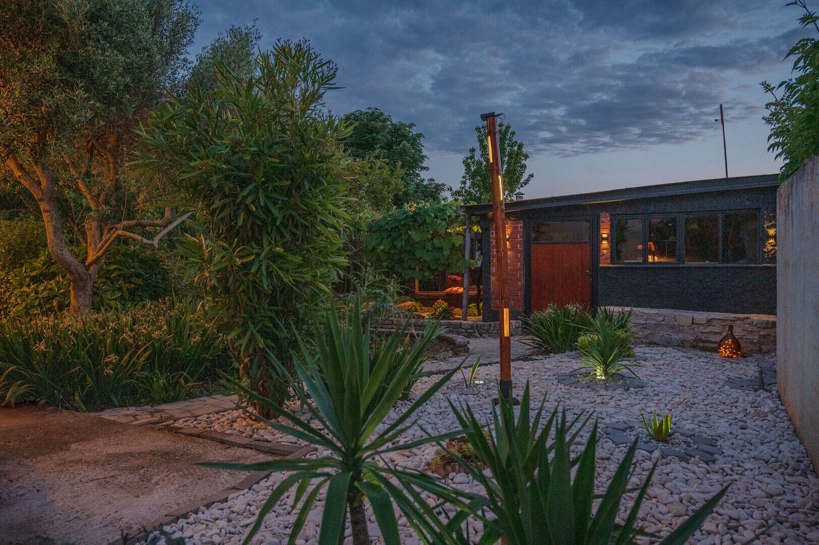 Een modern huis met een verharde oprit, omgeven door verschillende planten en bomen.