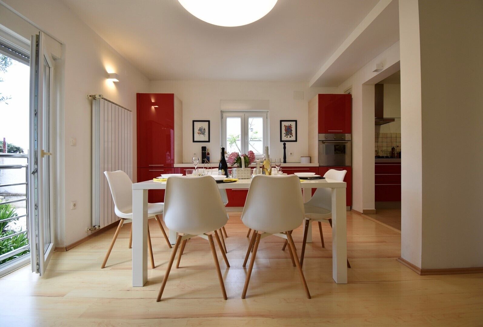 A modern kitchen with red cabinets, a dining area with white chairs, and a large window providing natural light.