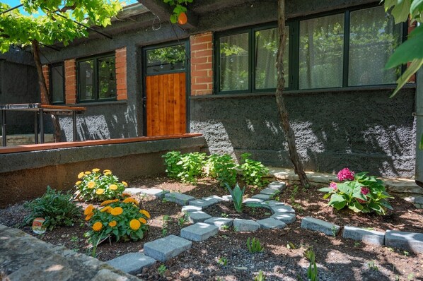A house with a brick exterior, a wooden door, and a garden with various plants and flowers.