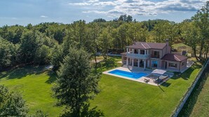 A large house with a swimming pool, surrounded by a well-maintained lawn and trees.