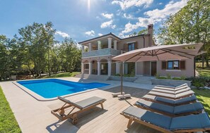 Una casa moderna de dos pisos con piscina, sillas de descanso al aire libre y un patio cubierto.