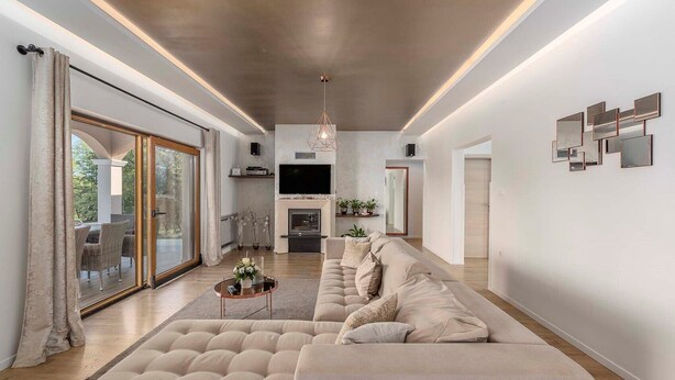 A modern living room with a large beige sectional sofa, a glass door leading to an outdoor area, a flat-screen TV, and a fireplace.