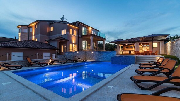 A swimming pool with lounge chairs, a covered seating area, and a building with multiple windows and balconies. - Villa Istrakamen in Valtura (Valtura)