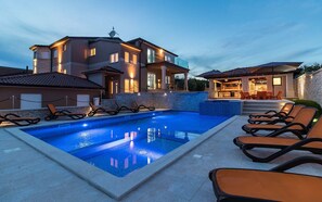 Une piscine avec des chaises longues, un espace de détente couvert et un bâtiment doté de nombreuses fenêtres et de balcons.