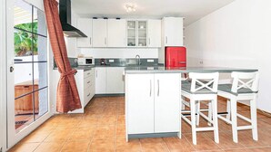 A kitchen with white cabinets, a red refrigerator, and a dining area with white chairs. - Paco Romo (Nerja)