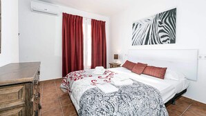 A bedroom with a bed, red curtains, a zebra print wall art, a wooden dresser, and a tiled floor. - Paco Romo (Nerja)