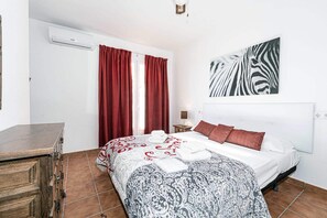 A bedroom with a bed, red curtains, a zebra print wall art, a wooden dresser, and a tiled floor. - Paco Romo (Nerja)