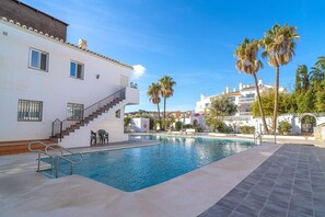 A swimming pool with a staircase leading to a building, palm trees, and a clear sky.
