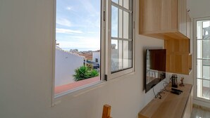 A room with a large window, a flat-screen TV, wooden cabinets, and a view of buildings. - Edf Papillon (Nerja)