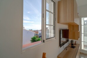 A room with a large window, a flat-screen TV, wooden cabinets, and a view of buildings.