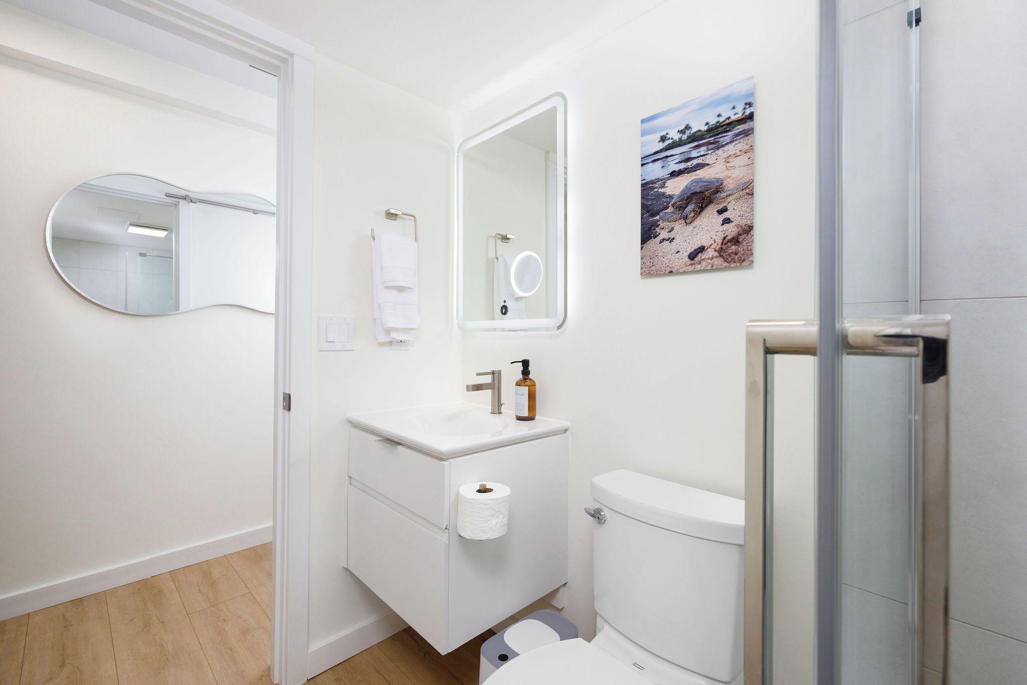 Un baño moderno con lavamanos blanco, inodoro y un espejo grande.