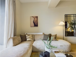 A modern living room with a sectional sofa, a glass coffee table, a floor lamp, and a framed abstract painting.