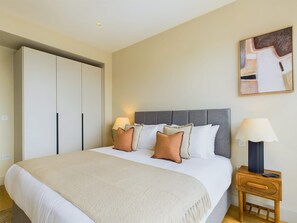 Quarto com cama, abajures, mesa de cabeceira e guarda-roupa.