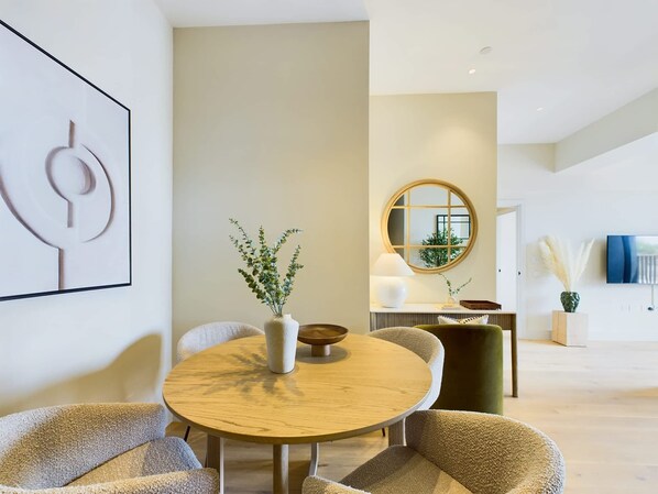 A modern living room with a round wooden table, comfortable seating, a decorative plant, a round mirror, and a television.