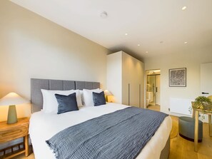 Una habitación de hotel moderna con una cama grande, lámparas de noche, un armario y un baño visible a través de una puerta abierta.