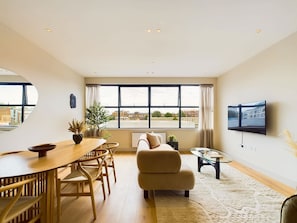 Una sala de estar moderna con comedor, ventanas amplias, televisor de pantalla plana y vistas de la ciudad.