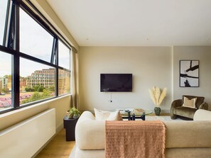 Ein modernes Wohnzimmer mit großem Fenster, Flachbildfernseher, Sofa, Couchtisch und Sessel.