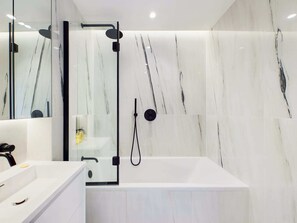 Ein modernes Badezimmer mit Duschkabine aus Glas, einer weißen Badewanne und Marmorwänden.