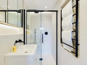 A modern bathroom with a glass-enclosed shower, a white sink, and a towel rack.