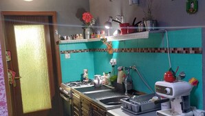 A kitchen with a gas stove, sink, and a coffee maker. There are various kitchen items on the counter and a decorative vase on the shelf. - Apartment Dario Šolta (Solta)