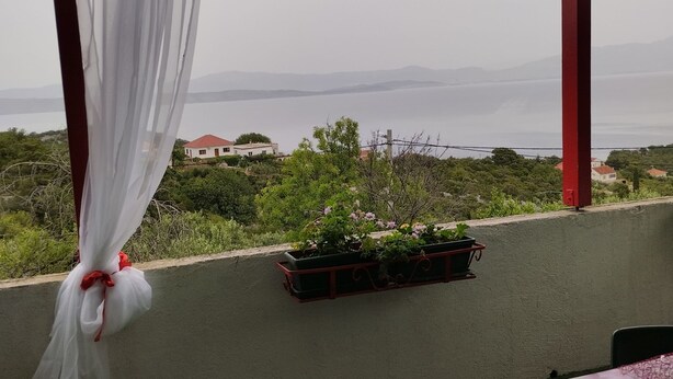 A balcony with a view of a distant landscape, a potted plant, and a white curtain. - Apartment Dario Šolta (Solta)