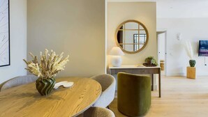 A modern dining area with a round table, chairs, a vase of dried flowers, a round mirror, and a small side table with a lamp. - Warm Relaxing St Pancras Apartment with Balcony (Greater London)