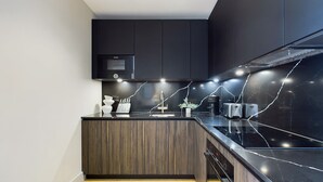 A modern kitchen with dark cabinetry, a built-in microwave, and a sleek countertop. - Warm Relaxing St Pancras Apartment with Balcony (Greater London)