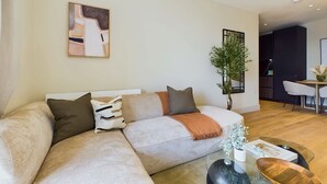 A modern living room with a sectional sofa, a glass coffee table, and a dining area in the background. - Warm Relaxing St Pancras Apartment with Balcony (Greater London)