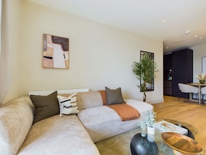 A modern living room with a sectional sofa, a glass coffee table, and a dining area in the background.