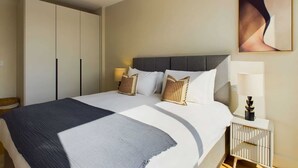 A hotel room with a bed, bedside tables, a wardrobe, and a painting on the wall. - Warm Relaxing St Pancras Apartment with Balcony (Greater London)