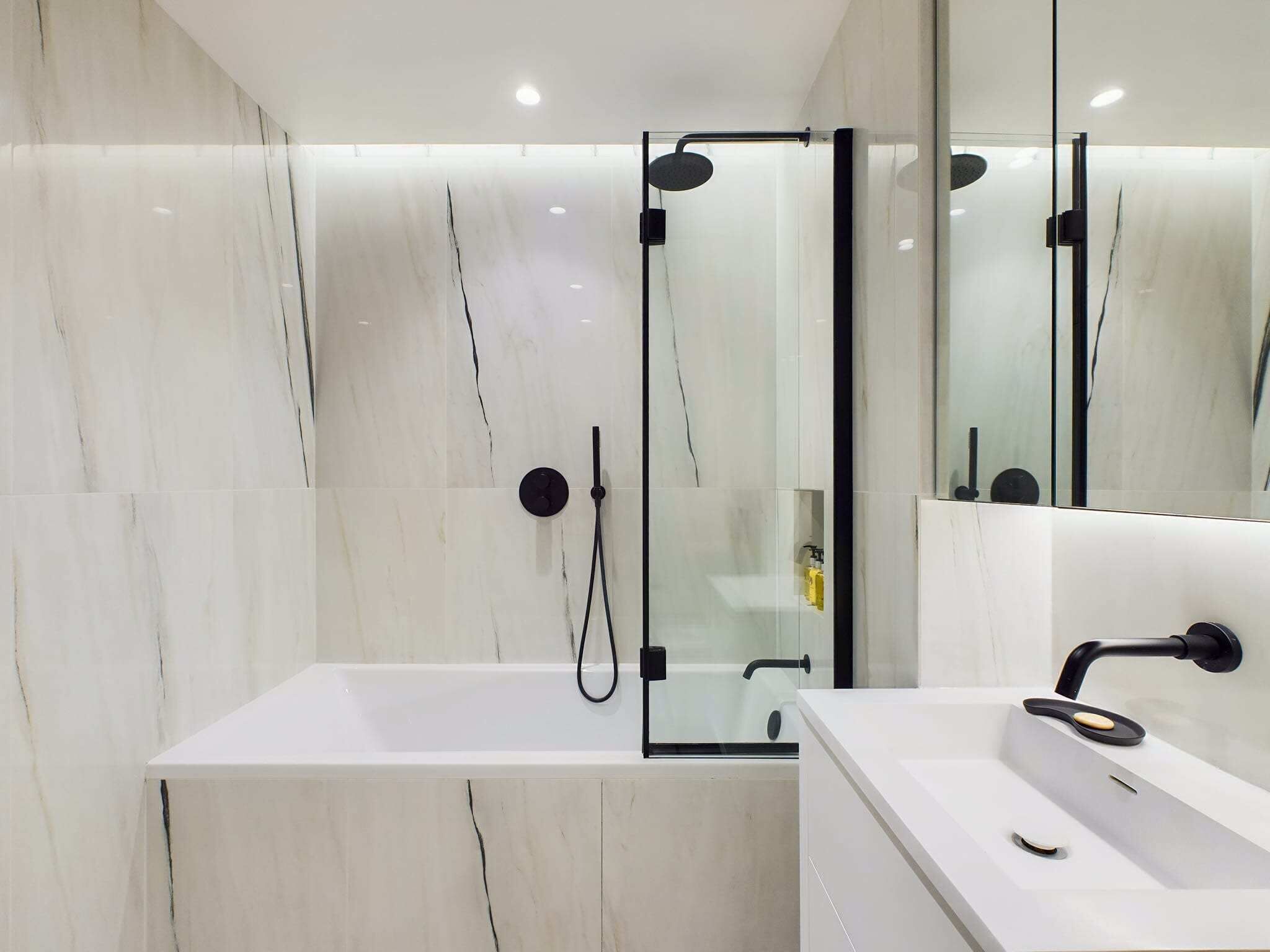 A modern bathroom with a glass-enclosed shower, a white bathtub, and a vanity with a mirror.