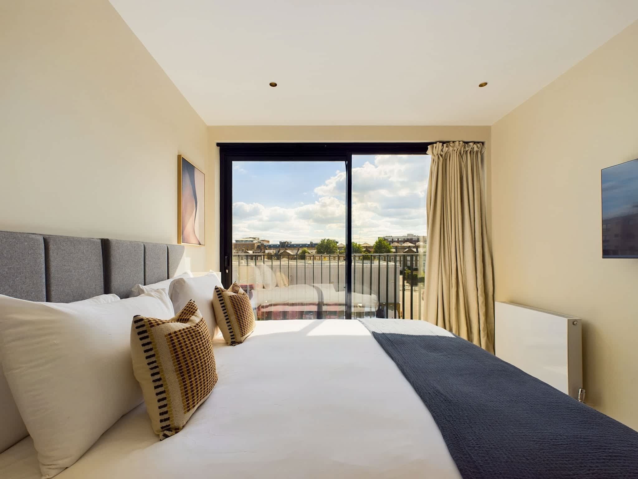 Ein Hotelzimmer mit einem großen Bett, Blick auf die Stadt und einem Balkon mit Geländer.