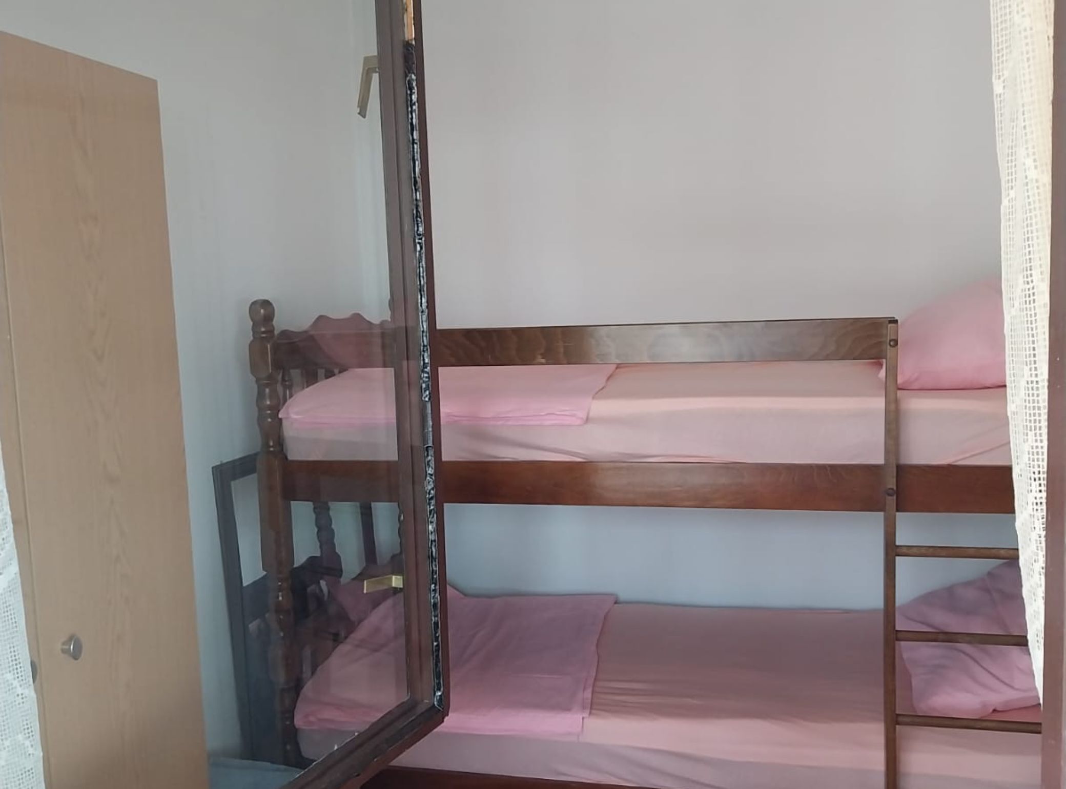 A bunk bed with pink bedding, a wooden headboard, and a mirror leaning against the wall.