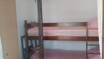 A bunk bed with pink bedding, a wooden headboard, and a mirror leaning against the wall.