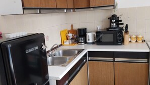 Une cuisine compacte équipée d’un réfrigérateur noir, d’un évier, d’un four à micro-ondes et d’une machine à café.