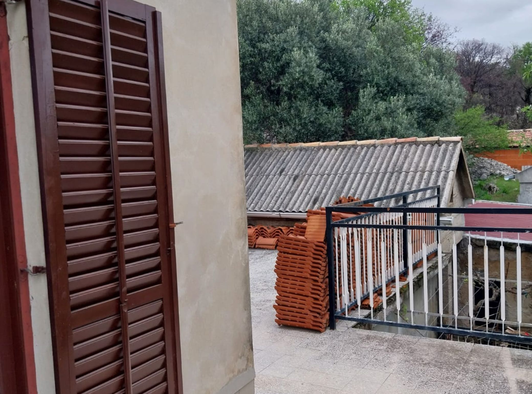 A balcony with a view of a garden and a tiled roof.