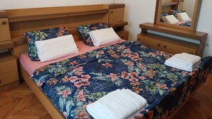 Un lit bien fait, avec une literie à motifs floraux, une table de chevet avec une lampe et un miroir au-dessus du lit.
