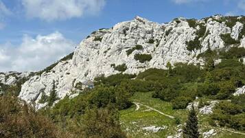 Paisaje montañoso con un pico rocoso, un edificio pequeño en la base y un cielo despejado.